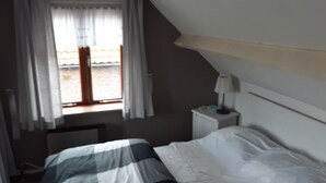 A bedroom with a bed, a window with curtains, a nightstand with a lamp, and a view of the outside. - nice cozy home (Sint-Annaland)