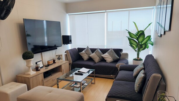 A modern living room with a flat-screen TV, a sofa set, a coffee table, and a potted plant. - Miraflores Apart near Kennedy Park+1Garage(11Persons/10Beds) (Miraflores)