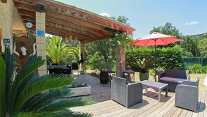 Eine Terrasse im Freien mit Korbmöbeln, einem roten Sonnenschirm und einer Uhr an der Wand.