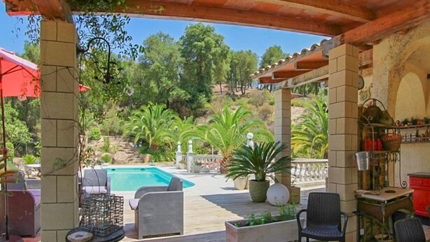 Eine Außenpatio-Terrasse mit Pool, Korbmöbeln und Topfpflanzen.