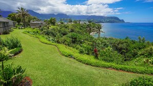 A lush garden with a pathway leading to a building, overlooking a clear blue ocean and distant mountains. - Pali Ke Kua 216 Amazing Panoramic View, idyllic retreat (Pinceville)