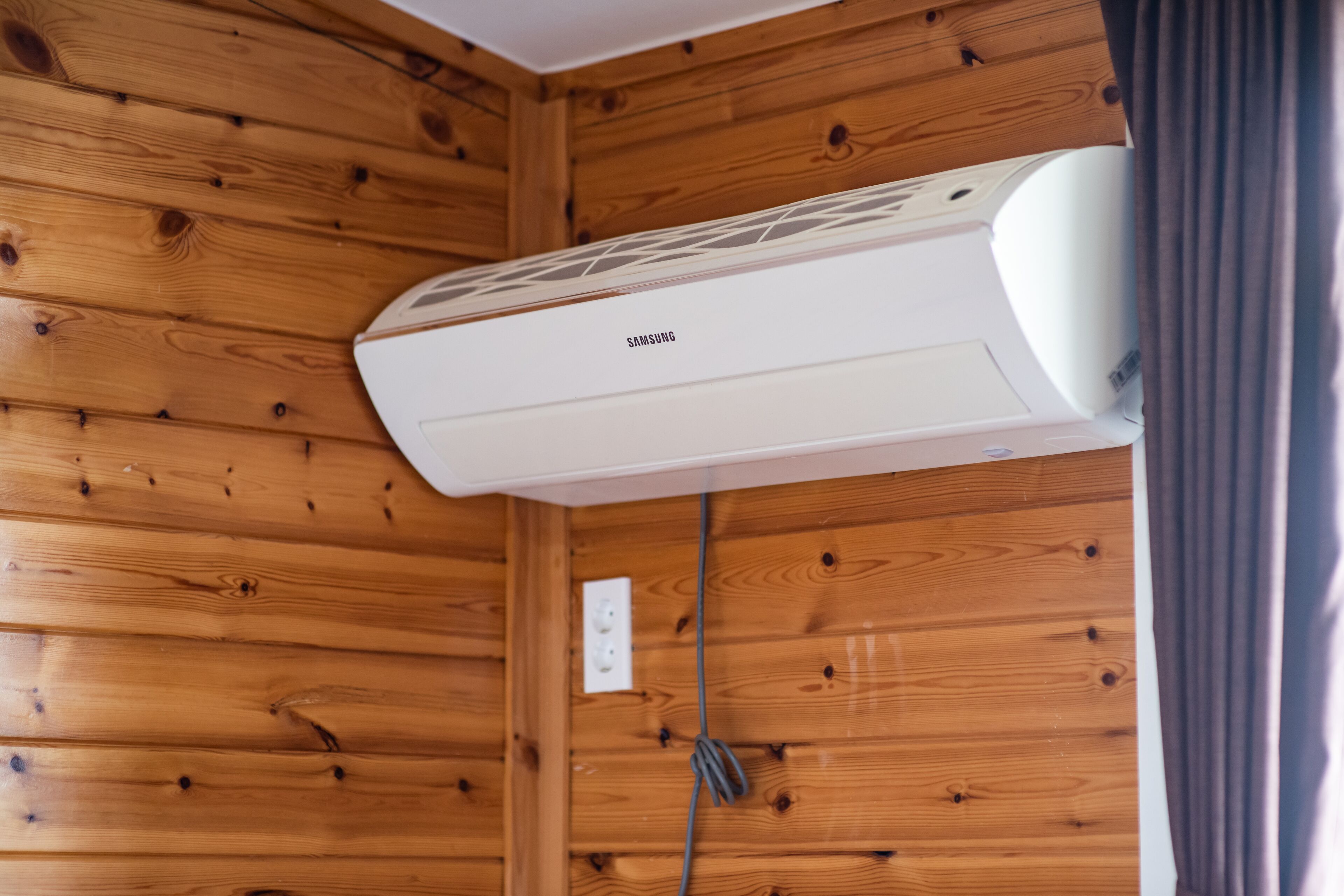 A white air conditioning unit mounted on a wooden wall in a cabin-style room.