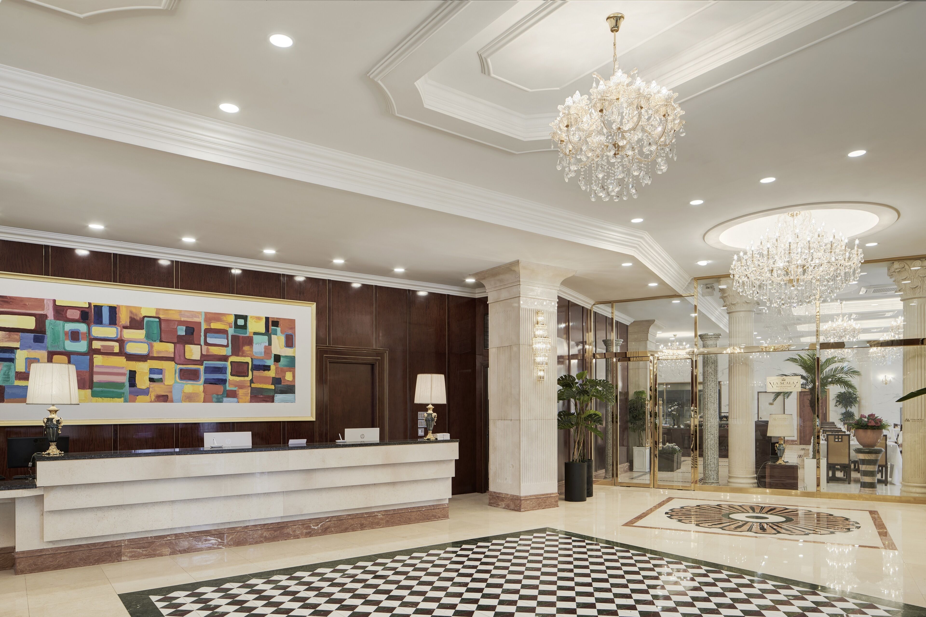 A hotel lobby with a reception desk, a checkered floor, and a large abstract painting.