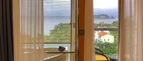 A bathroom with a bathtub, a towel rack, and a view of the sea and a distant island.