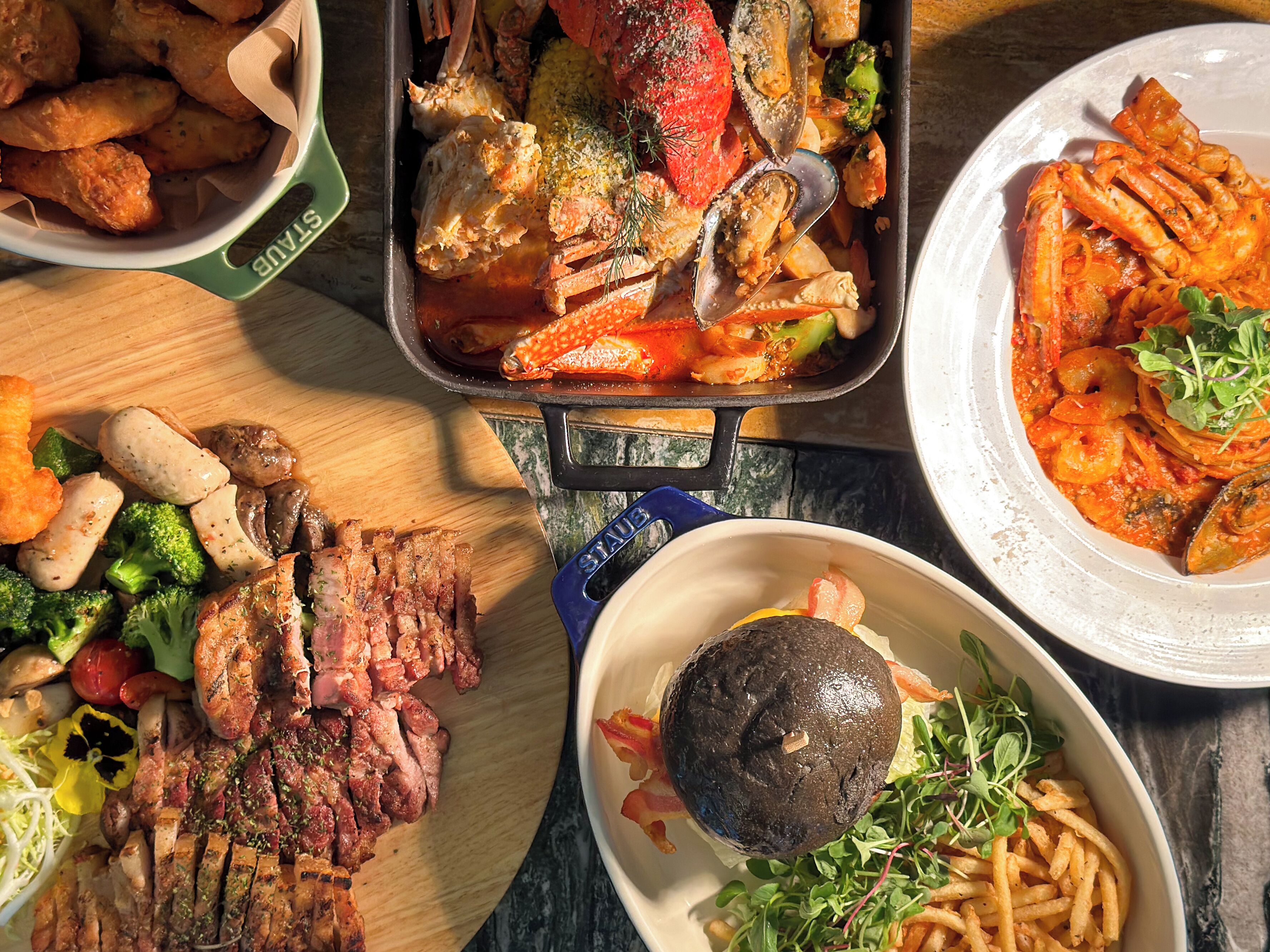 Una variedad de platos que incluyen mariscos, carnes a la parrilla y verduras sobre una mesa de madera.