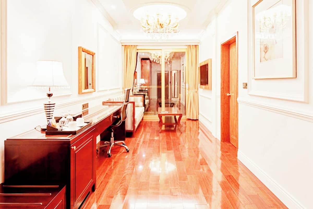 A hotel hallway with a wooden desk, a chair, a lamp, and a chandelier.