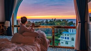 A room with a large window, a bed, and a view of a building and trees. - GoldOne Hotel & Suites (Seogwipo)