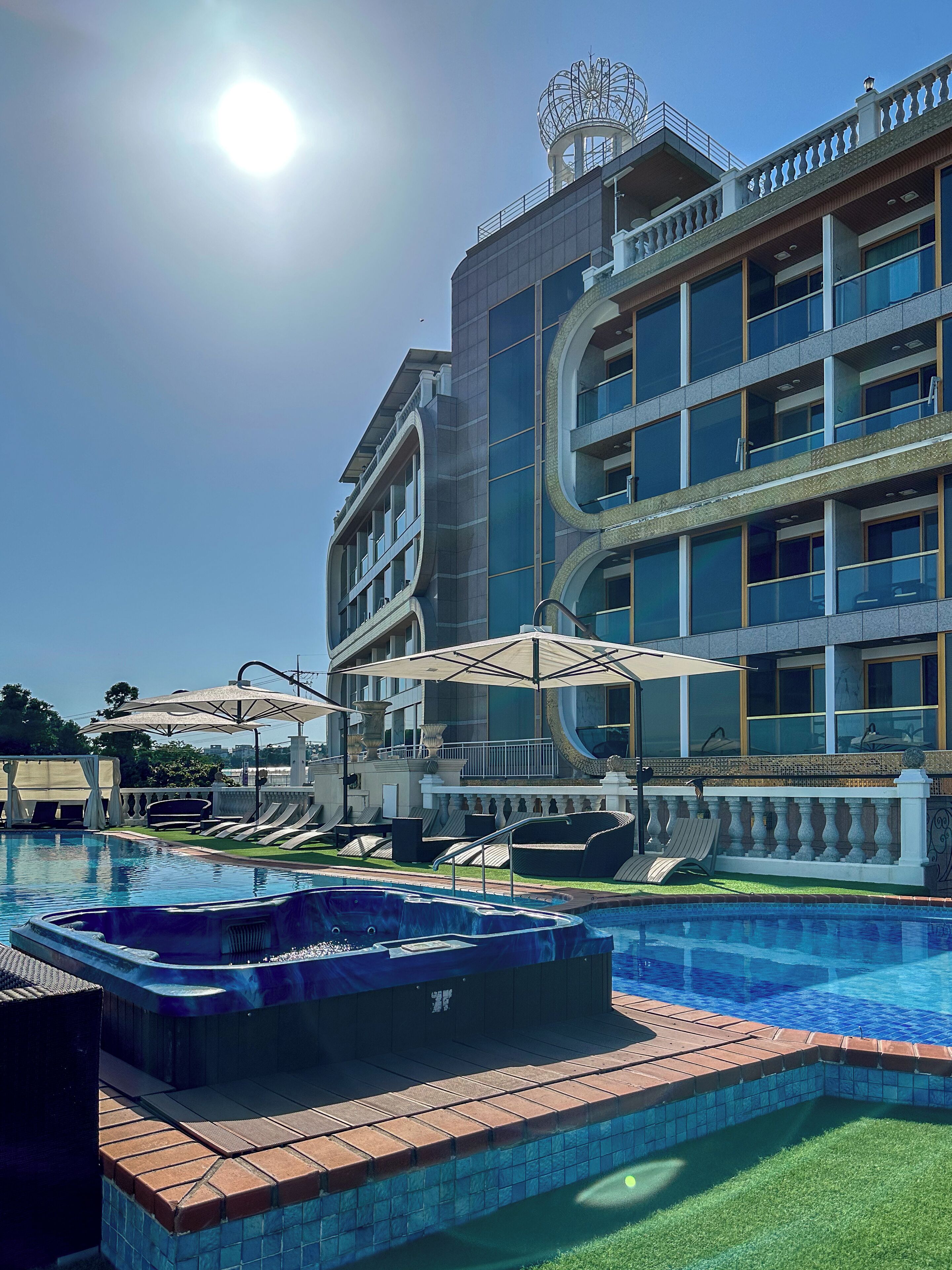 A hotel with a swimming pool, outdoor seating, and a large building with multiple balconies.