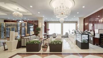 A spacious lobby with a checkered floor, a central seating area with sofas and chairs, a reception desk, and a large chandelier.