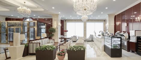 A spacious lobby with a checkered floor, a central seating area with sofas and chairs, a reception desk, and a large chandelier.