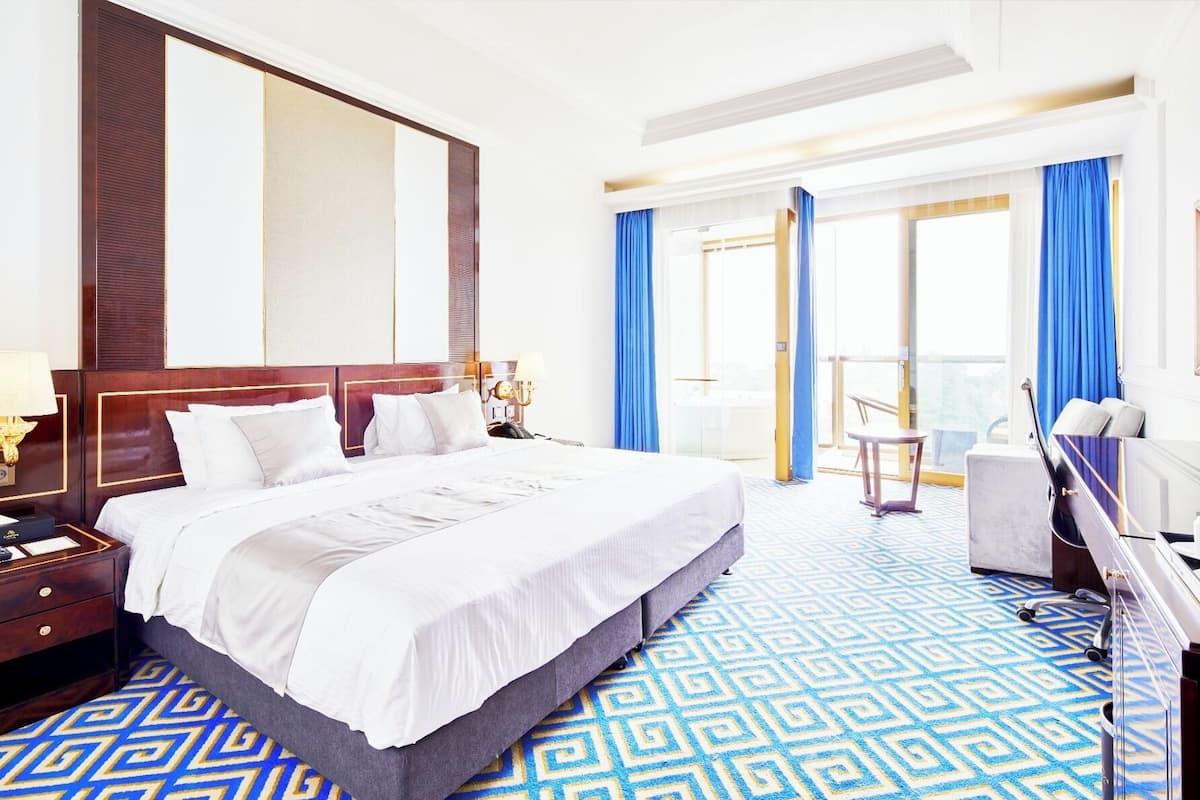 A hotel room with a large bed, a desk, a chair, and a view of the outside.