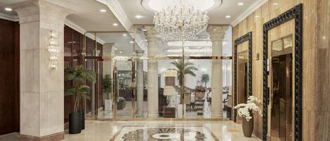 A grand lobby with a chandelier, marble flooring, and a large mirror.
