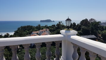 A balcony with a stone balustrade overlooking a coastal area with houses and a distant island.