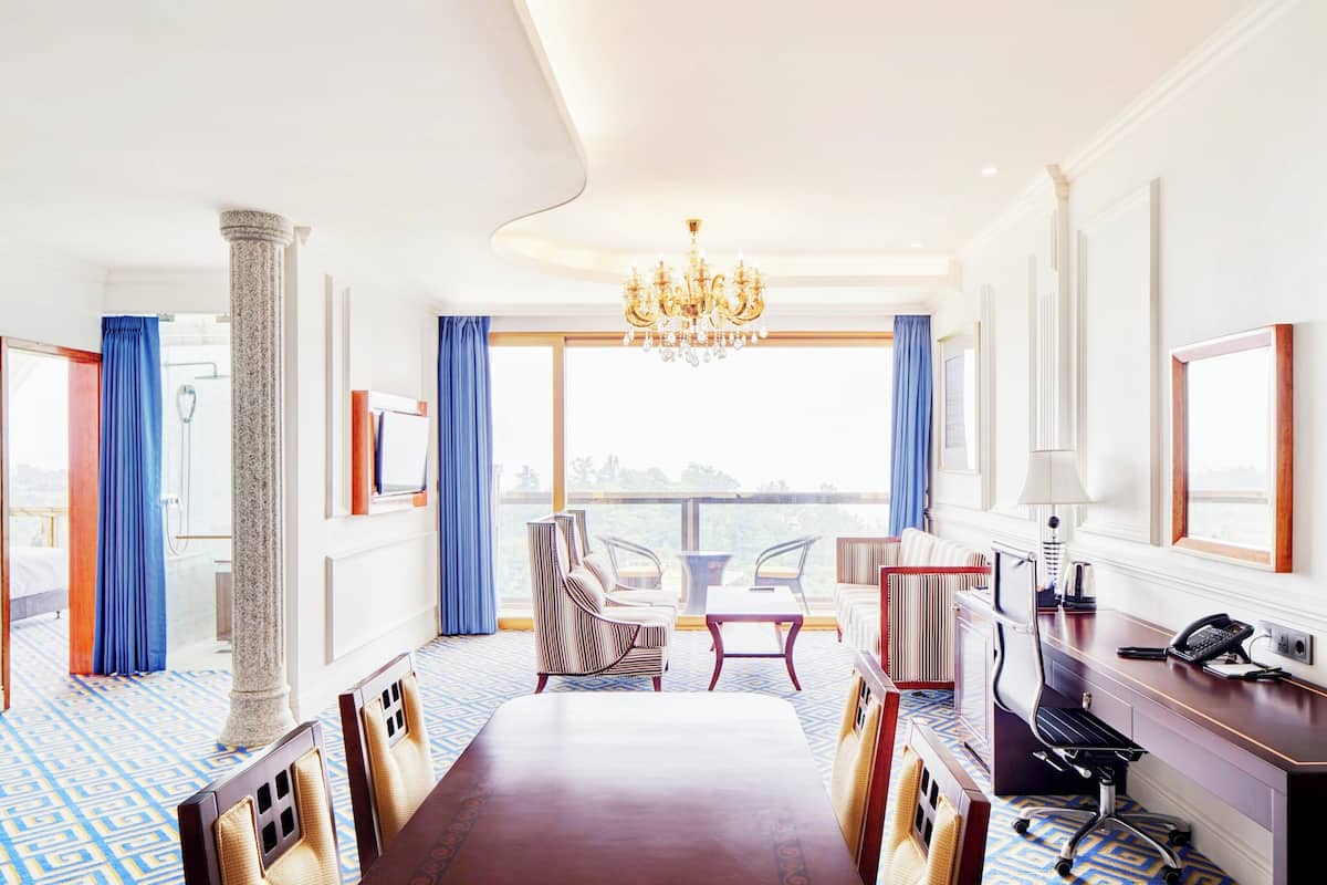 A hotel room with a large bed, a desk with a computer, a chair, a table, and a view of the outdoors.