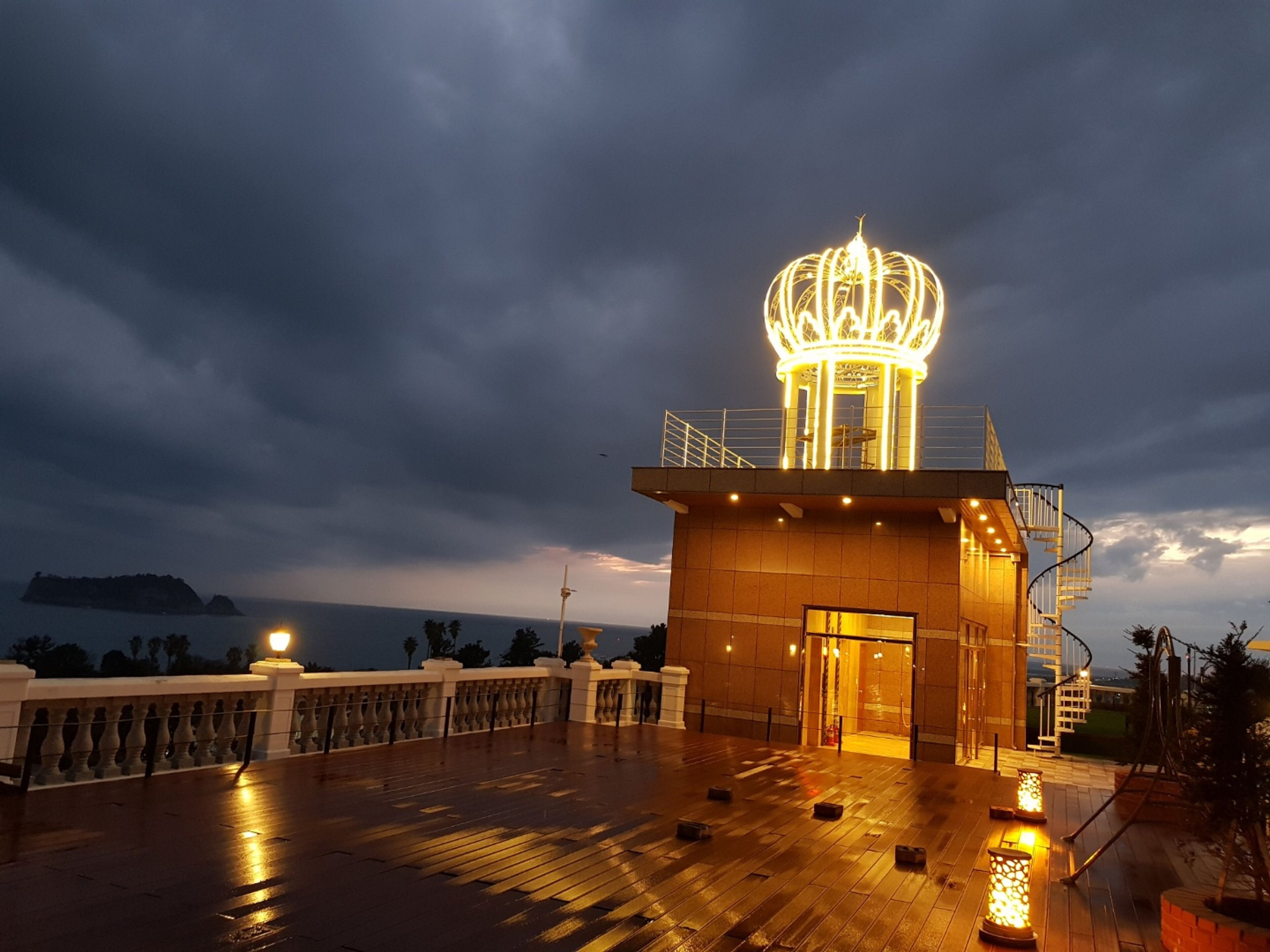 Una terraza en la azotea con una estructura luminosa central, una escalera de caracol y vistas al océano.
