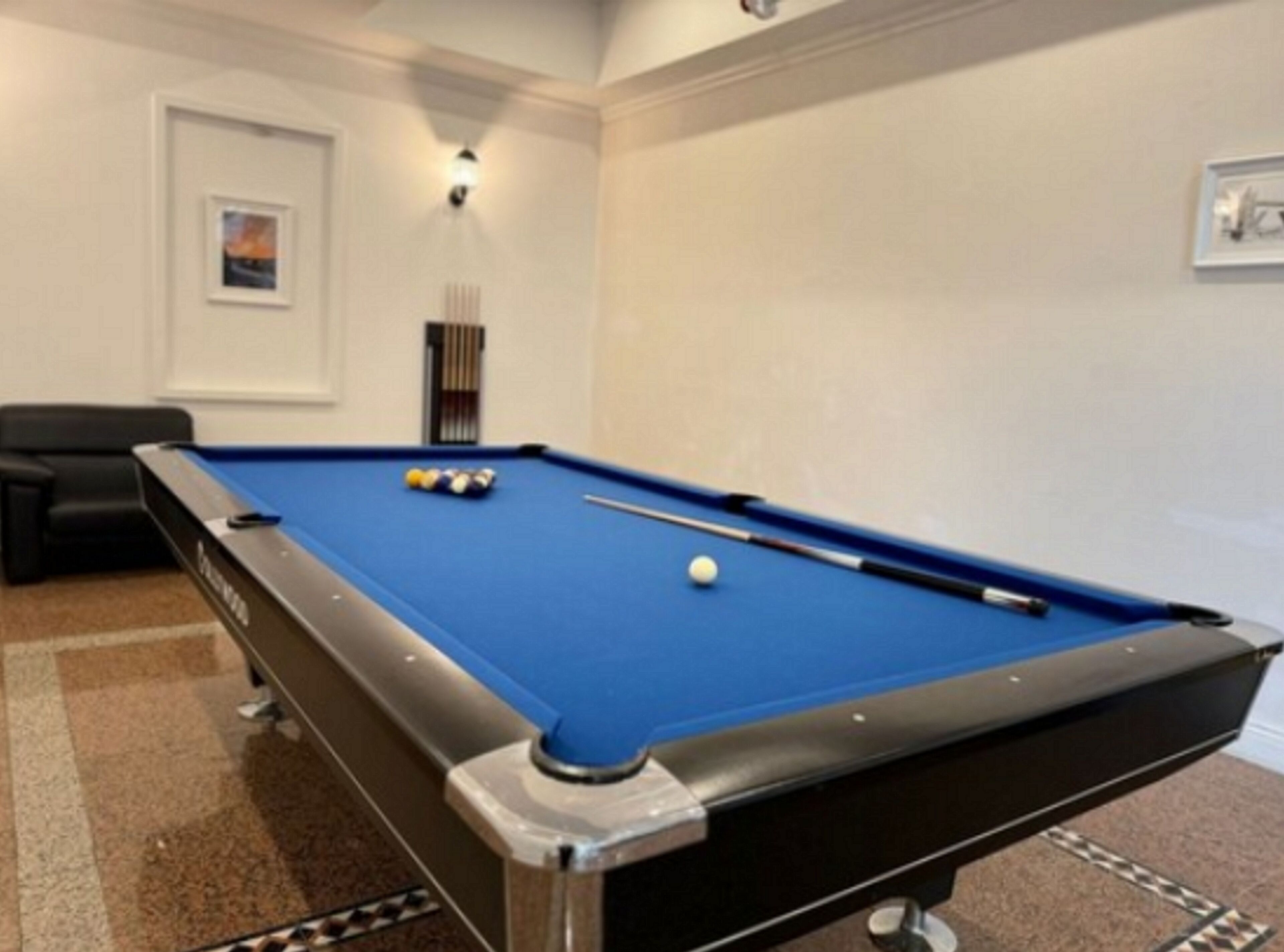A pool table with balls, a cue stick, and a framed picture on the wall.