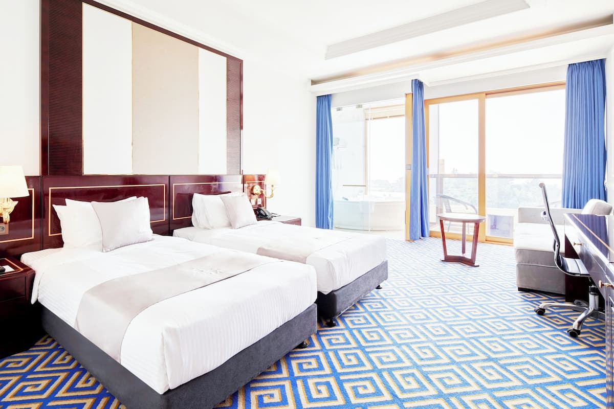A hotel room with two beds, a desk, and a large window with curtains.