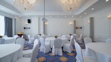 Un salón de conferencias con mesas redondas, sillas blancas y candelabros.