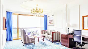 A hotel room with a large window, a chandelier, a sofa, a desk, and a chair.