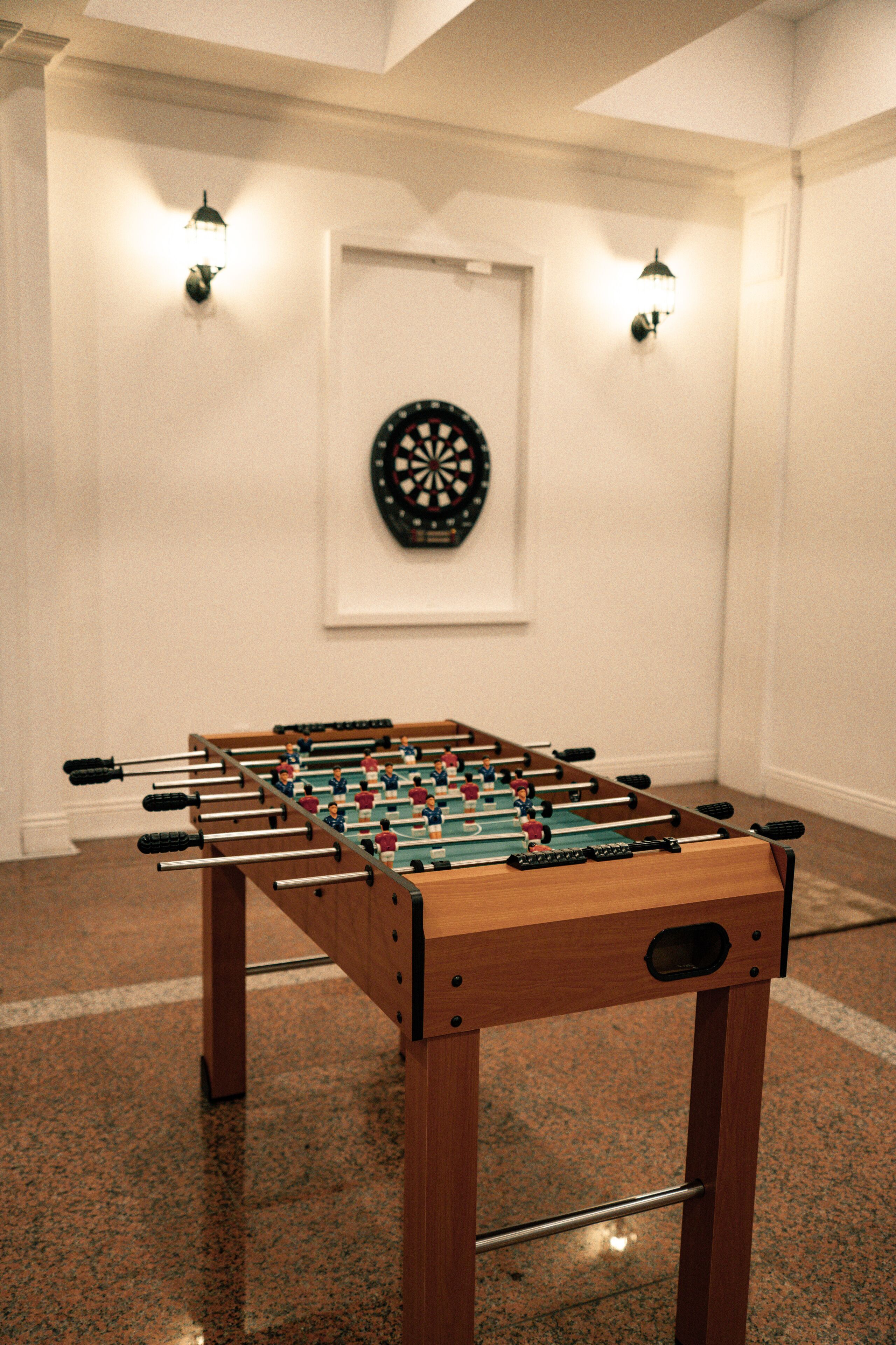 Taula de futbolí en una habitació amb una fletxa al mur i llums penjades a la paret.