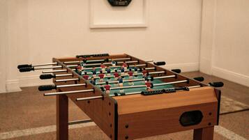 Uma mesa de futebol de mesa em um quarto com um alvo de dardos na parede e luminárias fixadas na parede.