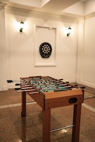 Uma mesa de futebol de mesa em um quarto com um alvo de dardos na parede e luminárias fixadas na parede.
