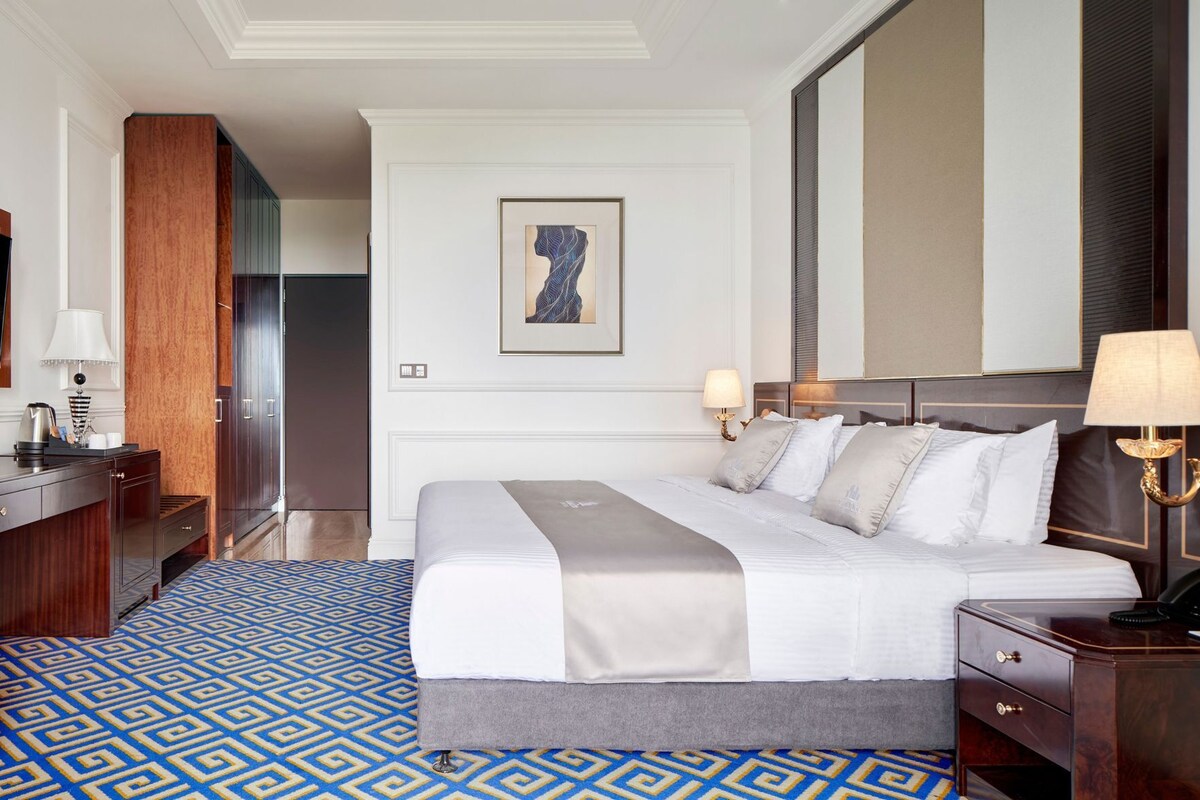 A hotel room with a large bed, bedside tables, a desk, and a mirror.