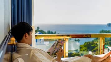 Una persona recostada en una cama junto a una ventana, leyendo un libro.