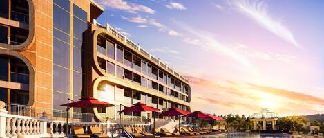 A hotel with a swimming pool, sun loungers, and umbrellas.