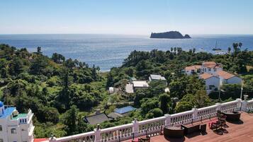A terrace with outdoor seating overlooking a coastal area with buildings and greenery.