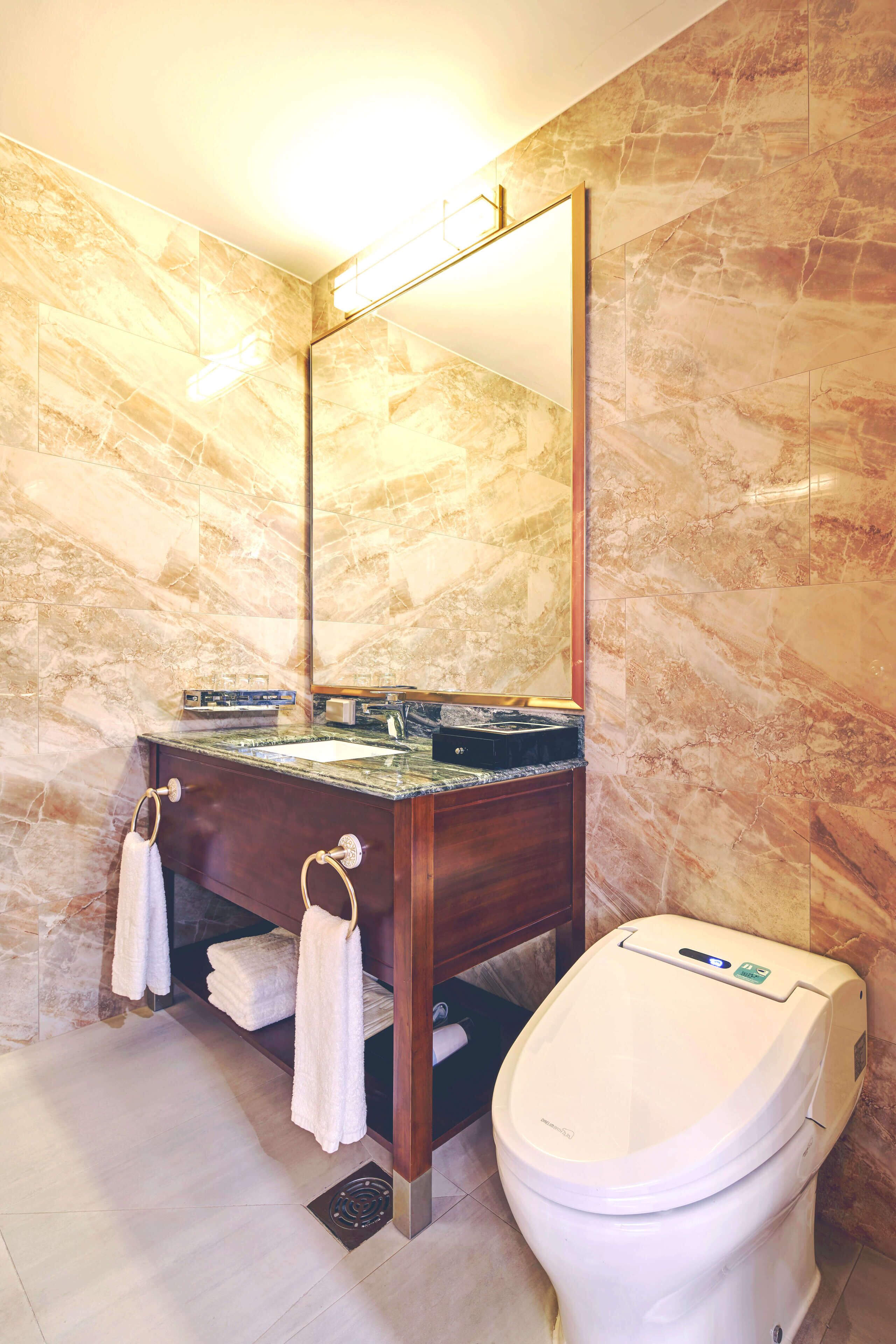 A bathroom with a marble wall, a wooden vanity, a sink, a toilet, and a mirror.
