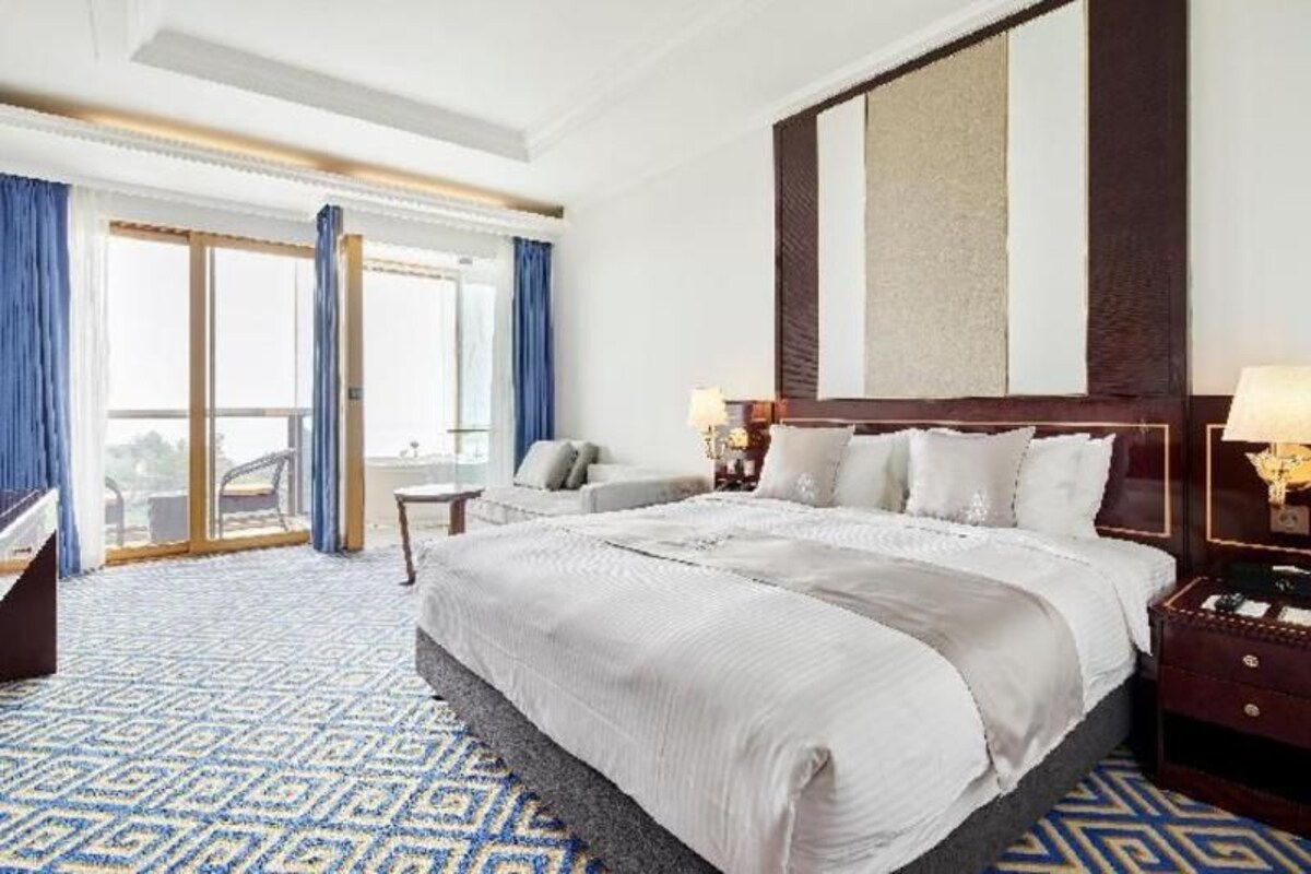 A hotel room with a large bed, a desk, a chair, and a view through a glass door.
