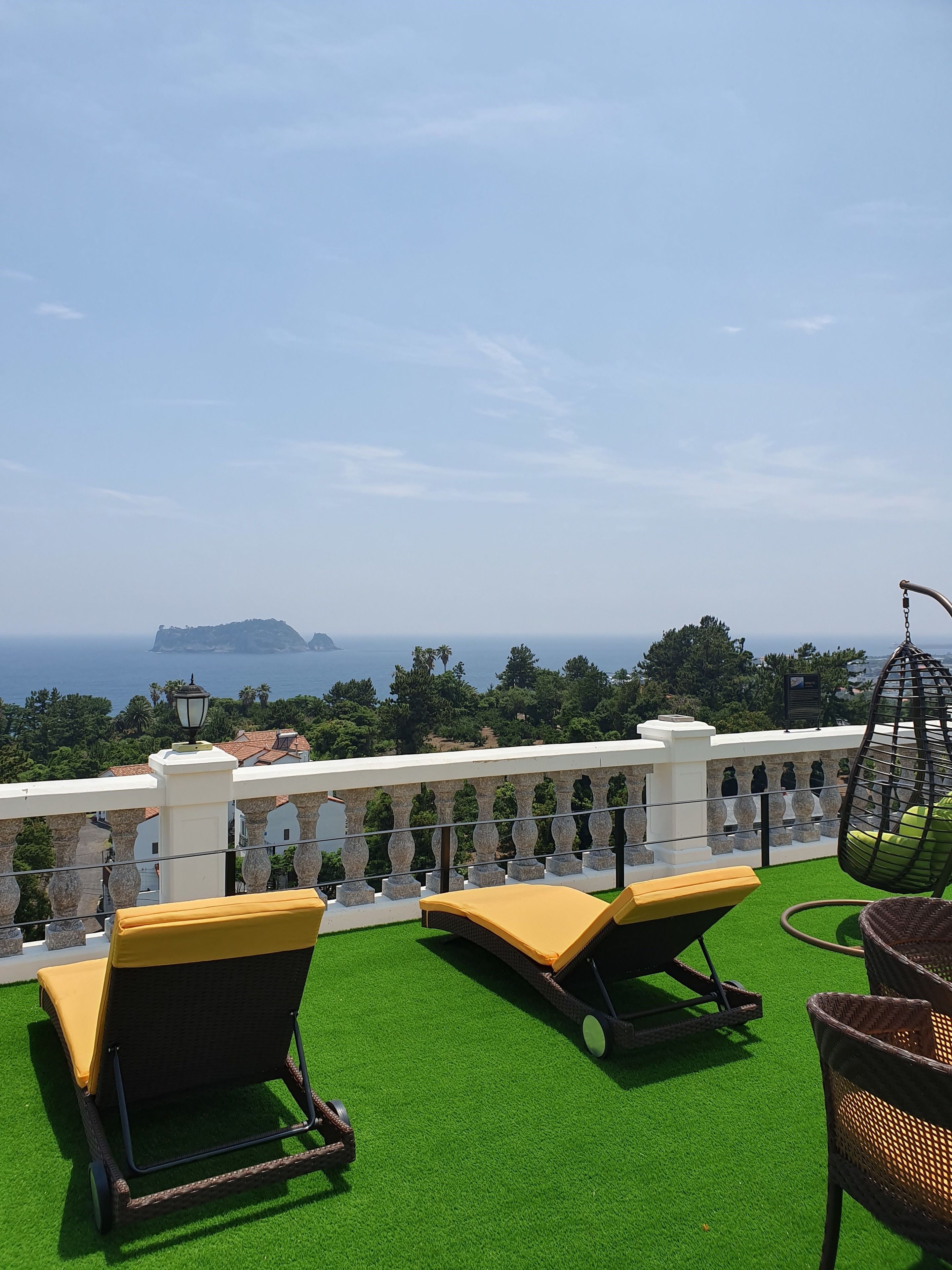 A terrace with two lounge chairs and a hanging chair, overlooking a coastal landscape with a distant island.