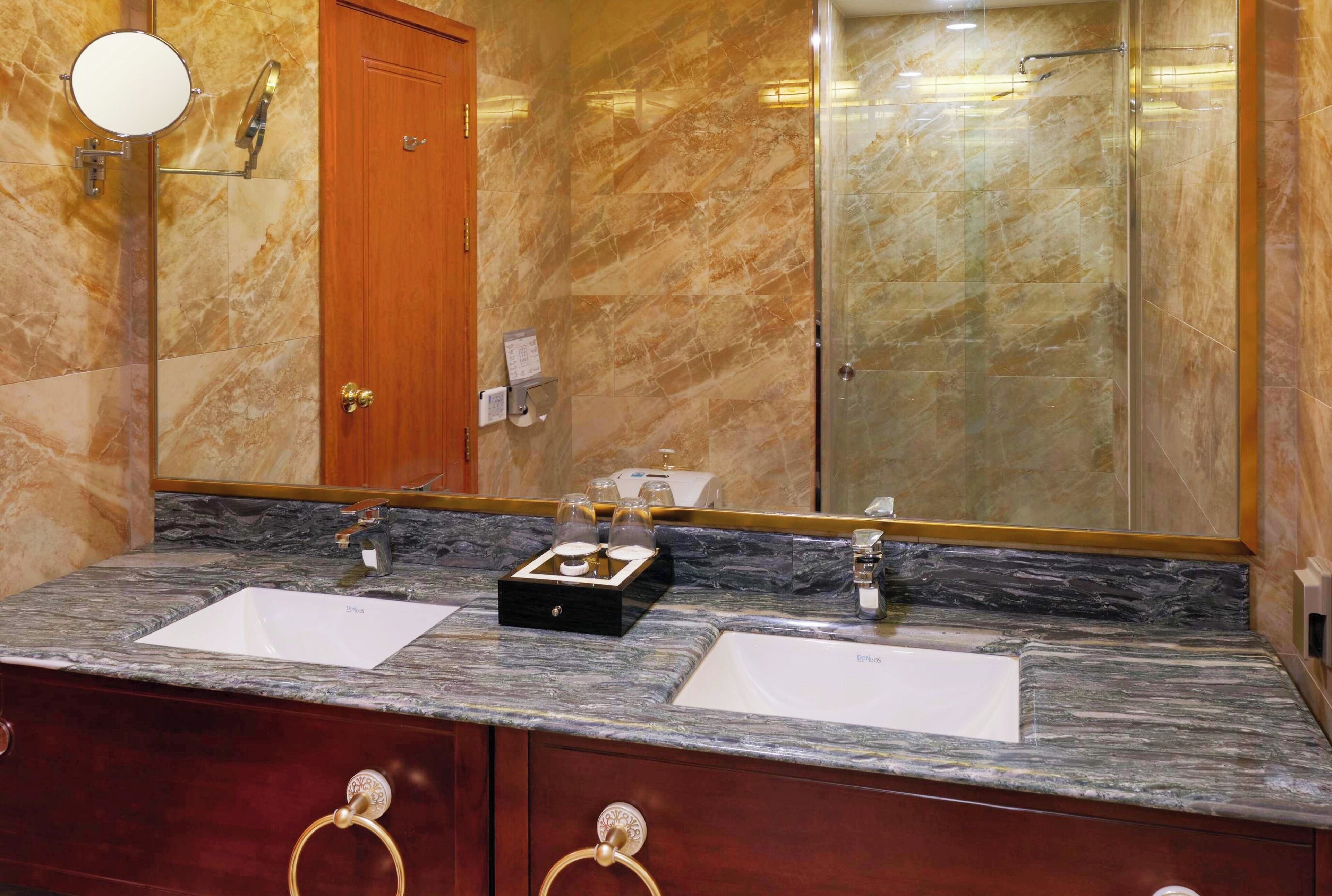 A bathroom with two sinks, marble countertops, a wooden door, and a large mirror.