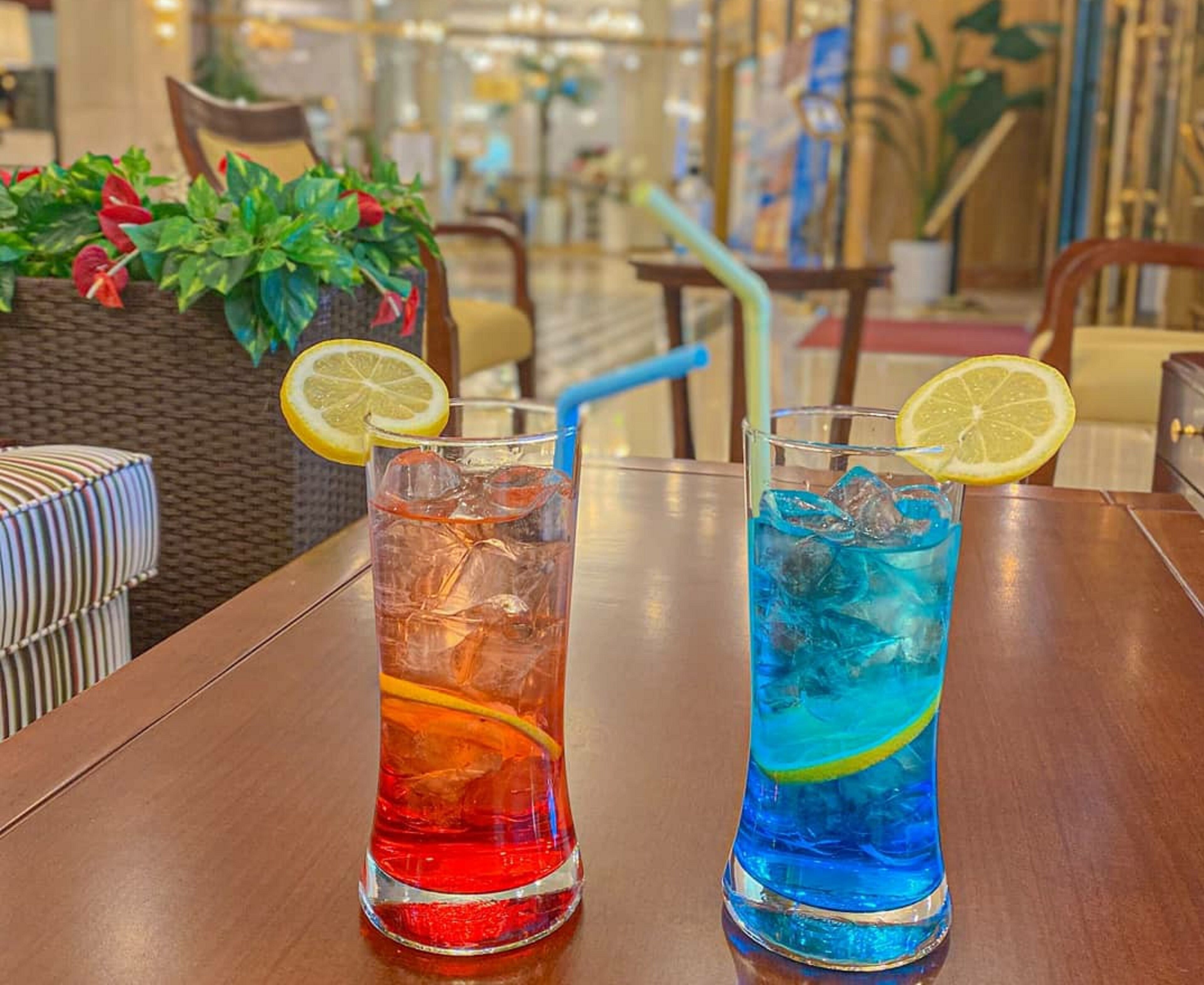 Two drinks on a table with a wicker chair and a striped cushion in the background.