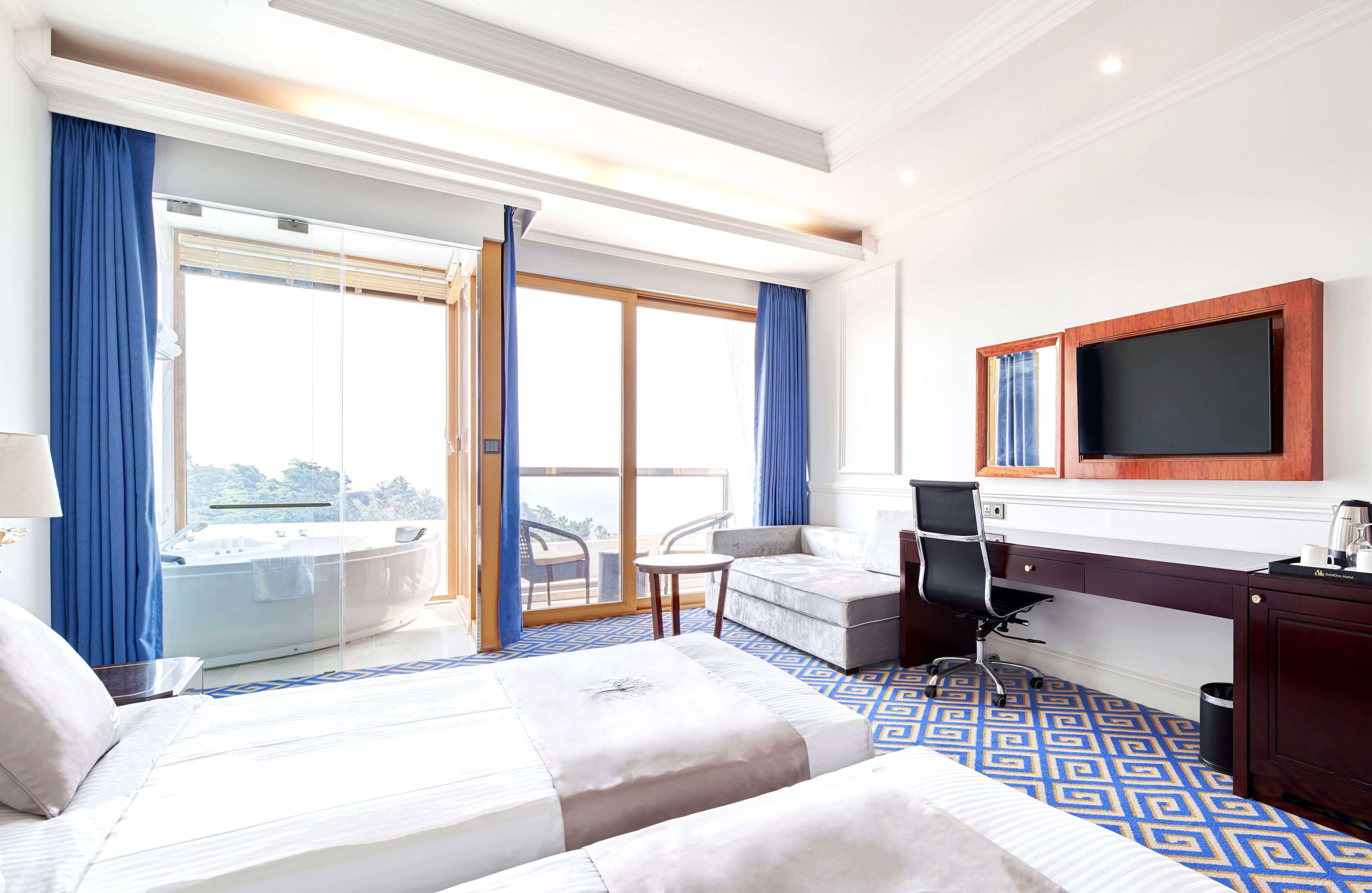 A hotel room with a large bed, a desk with a computer, a TV mounted on the wall, and a balcony with a hot tub.