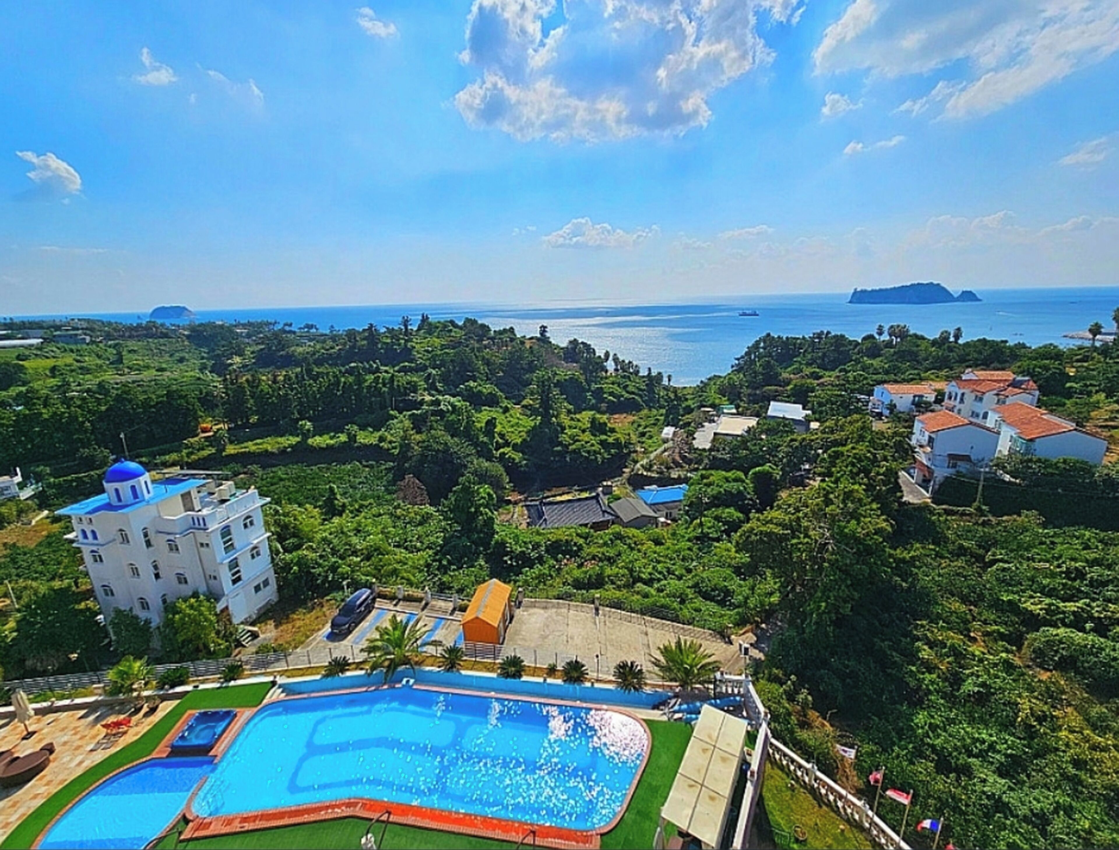 A resort with a large swimming pool, lush greenery, and a view of the sea.