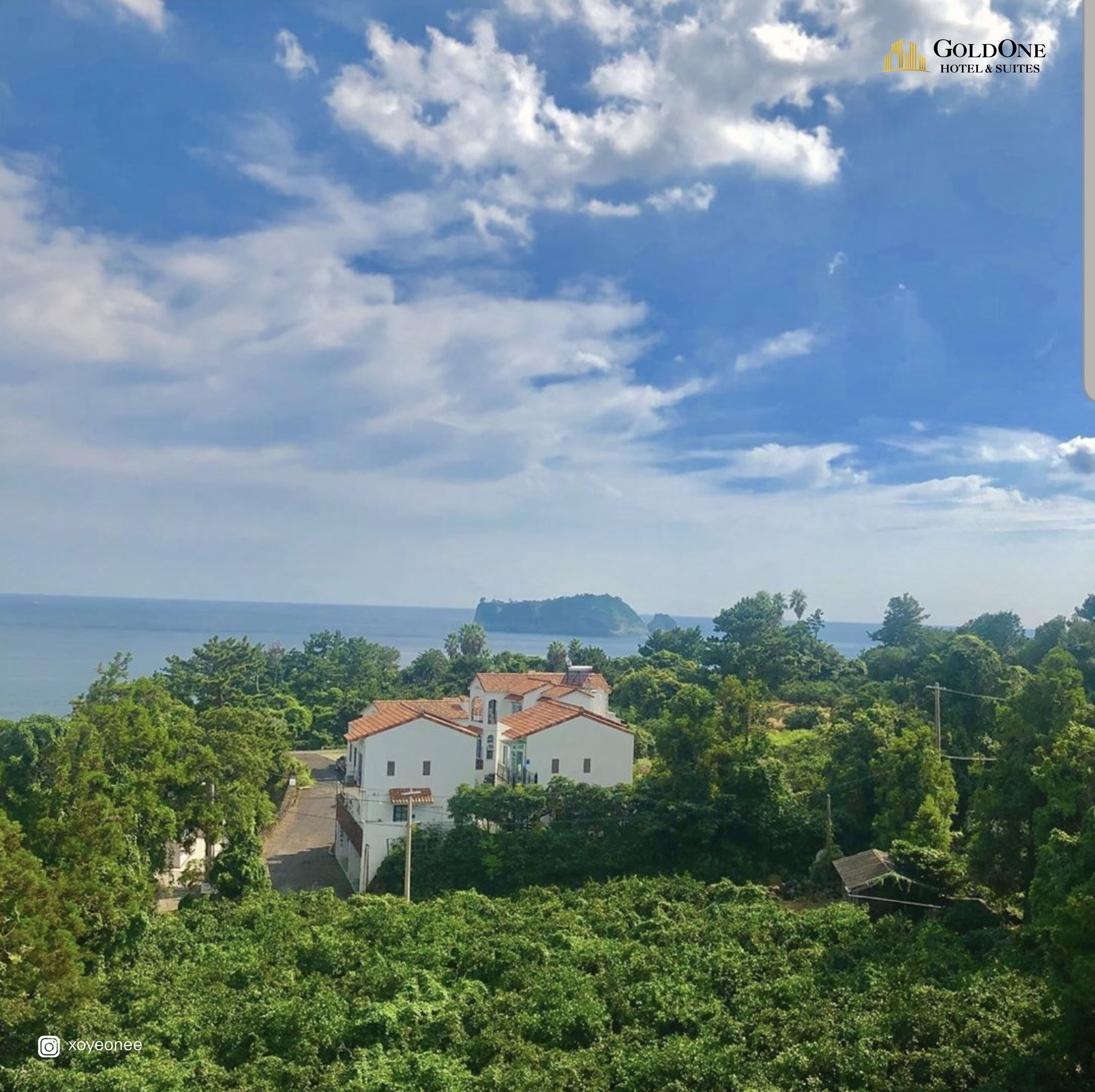 Una propiedad costera con un edificio blanco de tejado rojo, rodeada de exuberante vegetación y con vistas al mar.