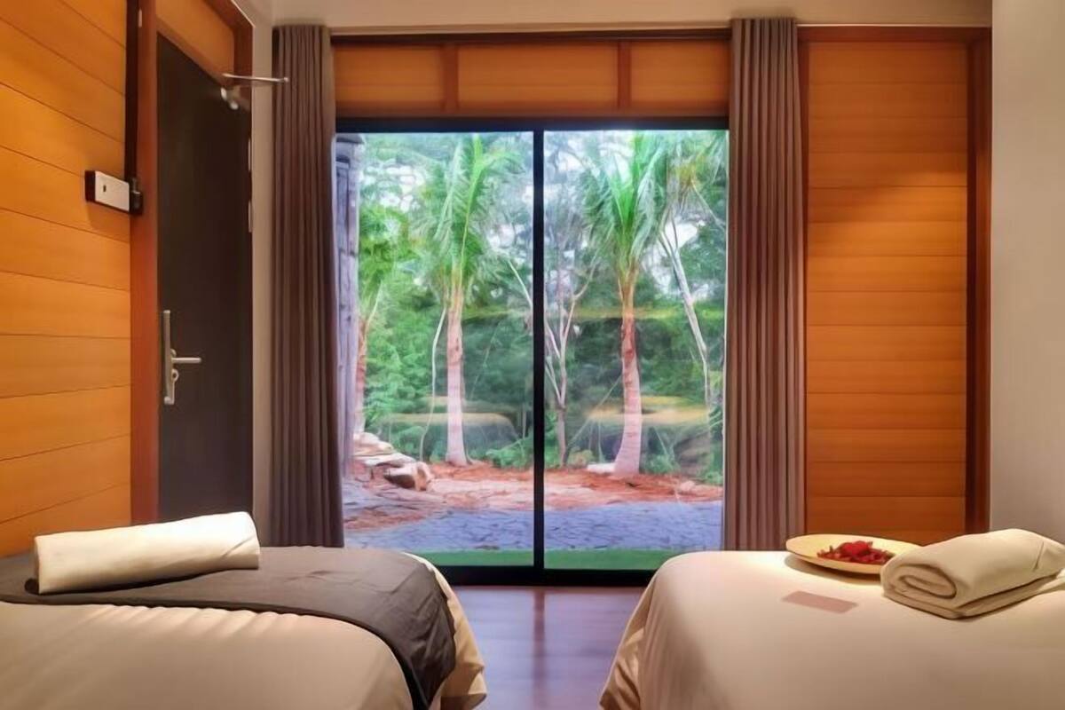 Ein Zimmer mit zwei Betten, einer Schiebetür und Blick auf einen tropischen Garten sowie einem kleinen Tisch mit einer Teller voller Essen.