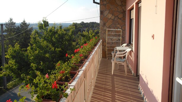 A balcony with a stone wall, a metal drying rack, and white plastic chairs. - Apartments in Heviz / Thermal Lake / Hungary (HÉVÍZ)
