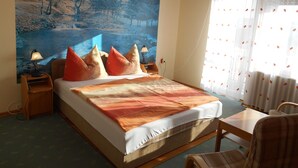 A bedroom with a bed, a nightstand, a lamp, a chair, a table, and a large painting on the wall. - Apartments in Heviz / Thermal Lake / Hungary (HÉVÍZ)