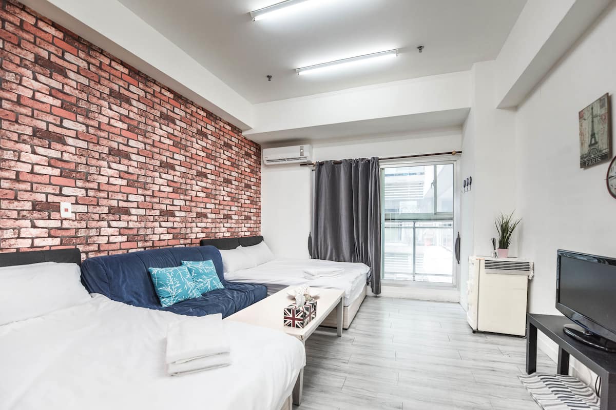 A modern hotel room with a brick accent wall, a sofa bed, a TV, and a small table.