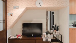A living room with a flat-screen TV on a wooden stand, a clock on the wall, and a small table with decorative items. - Love Taipei - Ximen (Taipei)