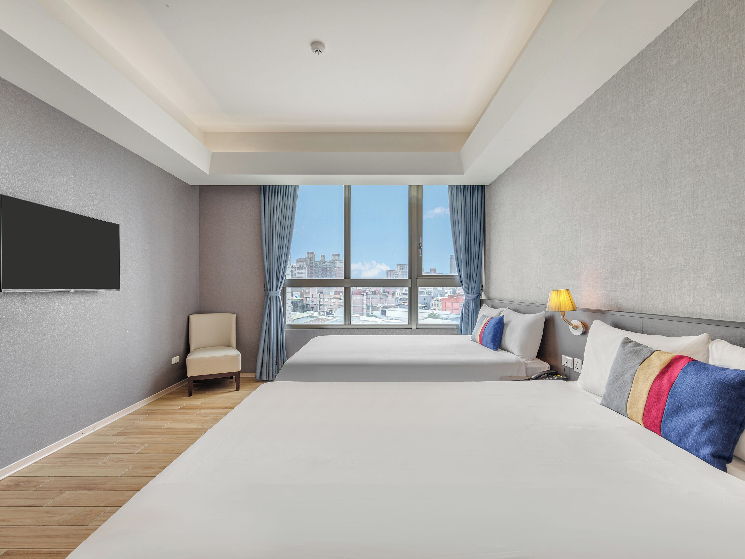A hotel room with a large bed, a chair, a television, and a window with a city view.