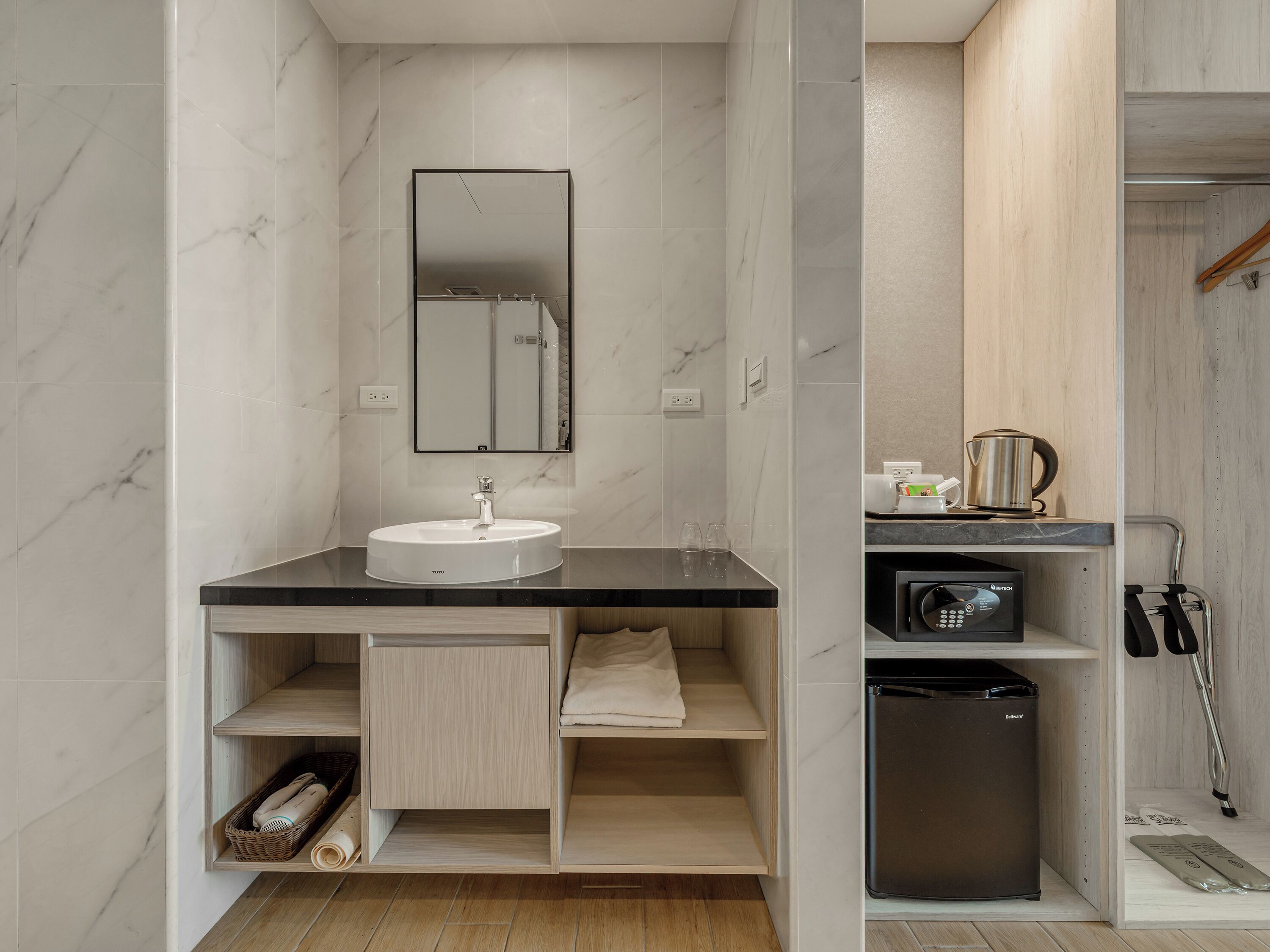 A modern bathroom with a marble sink, a mirror, a towel rack, a small cabinet, and a compact refrigerator.