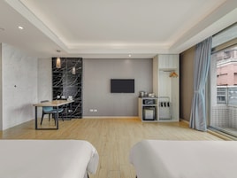 Habitación de hotel moderna con televisión de pantalla plana, zona de comedor, kitchenette y balcón con vistas.
