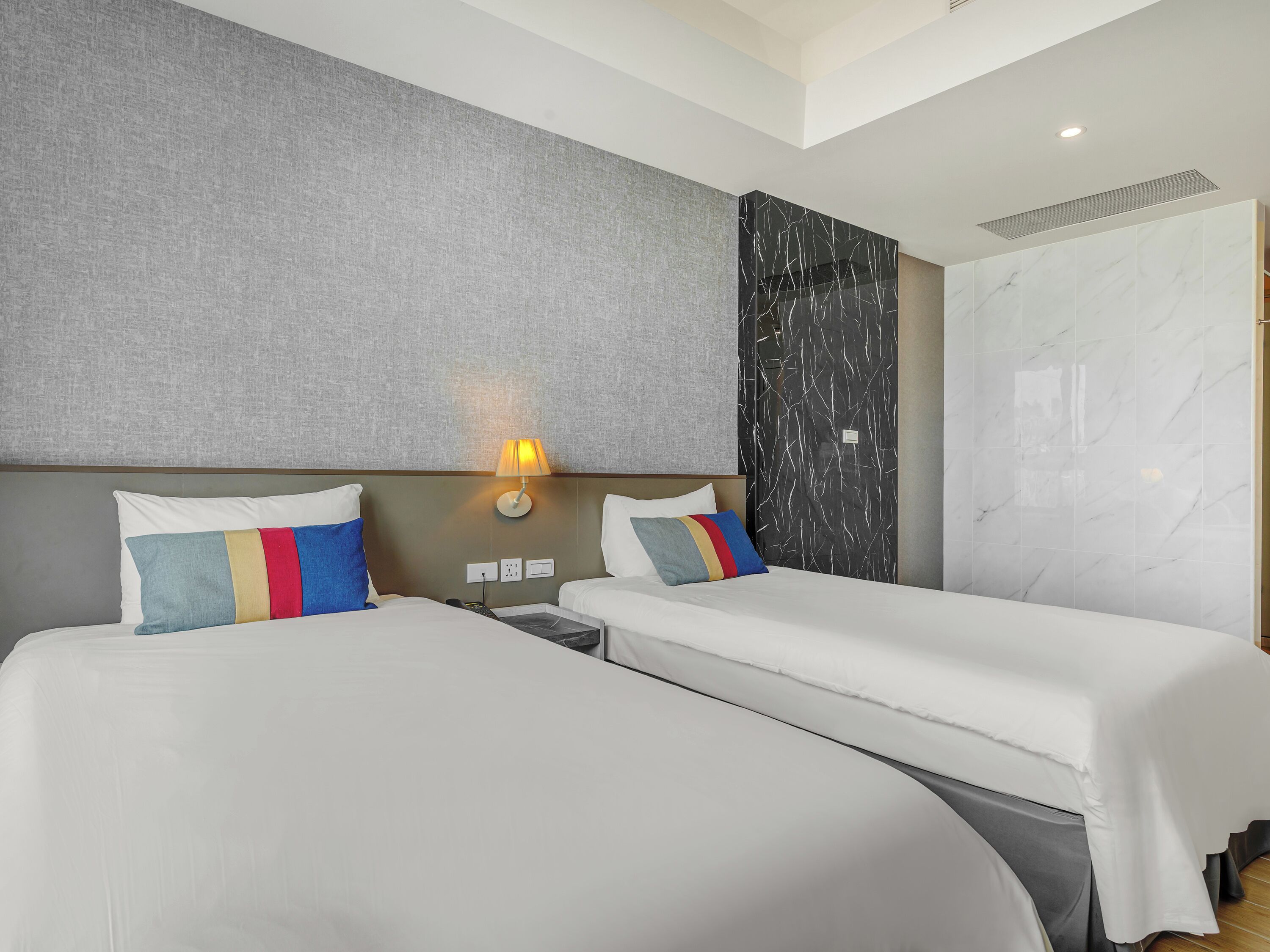 A hotel room with two beds, a wall-mounted lamp, and a large wardrobe.