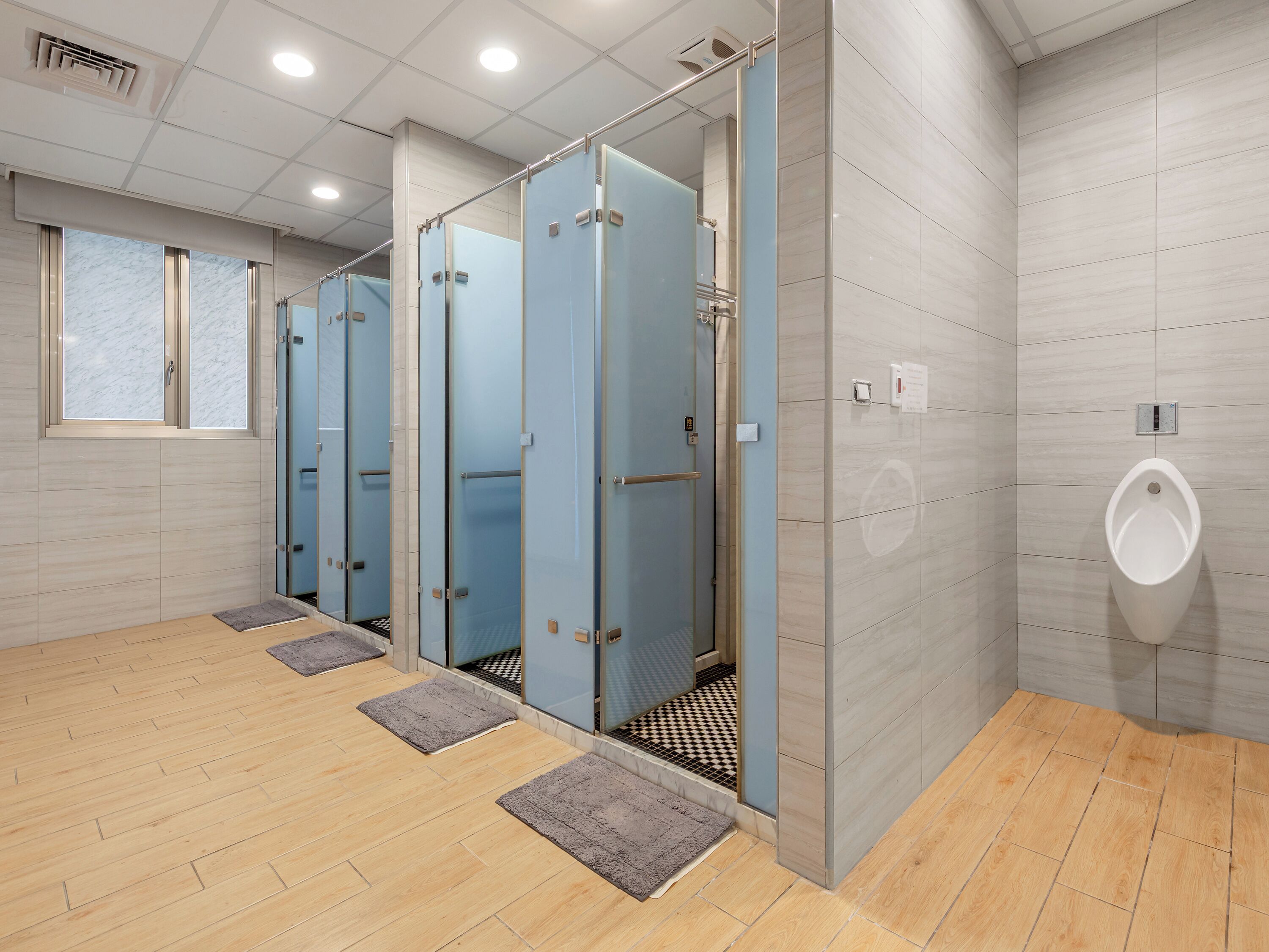 A modern restroom with multiple stalls, a urinal, and a checkered floor pattern.