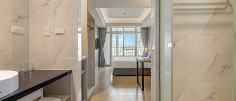A hotel room with a bathroom, a bed, a TV, and a view of the city.