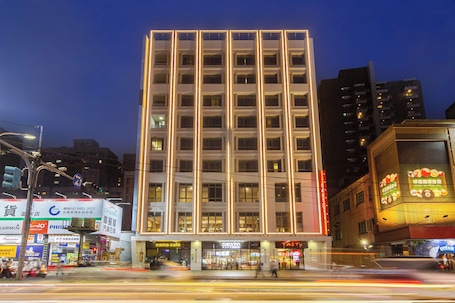 A modern multi-story building with illuminated windows and a prominent entrance.